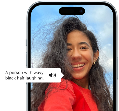 Widoczny na ekranie iPhone’a 15 komunikat VoiceOver z następującym opisem zdjęcia: śmiejąca się osoba z falowanymi czarnymi włosami