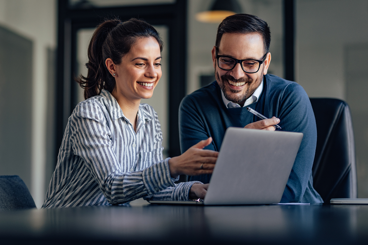 Dwoje uśmiechniętych ludzi patrzących w&nbsp;ekran laptopa