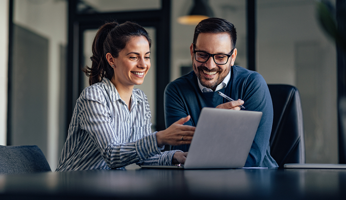 Kobieta i mężczyzna uśmiechnięci patrzą w ekran laptopa.