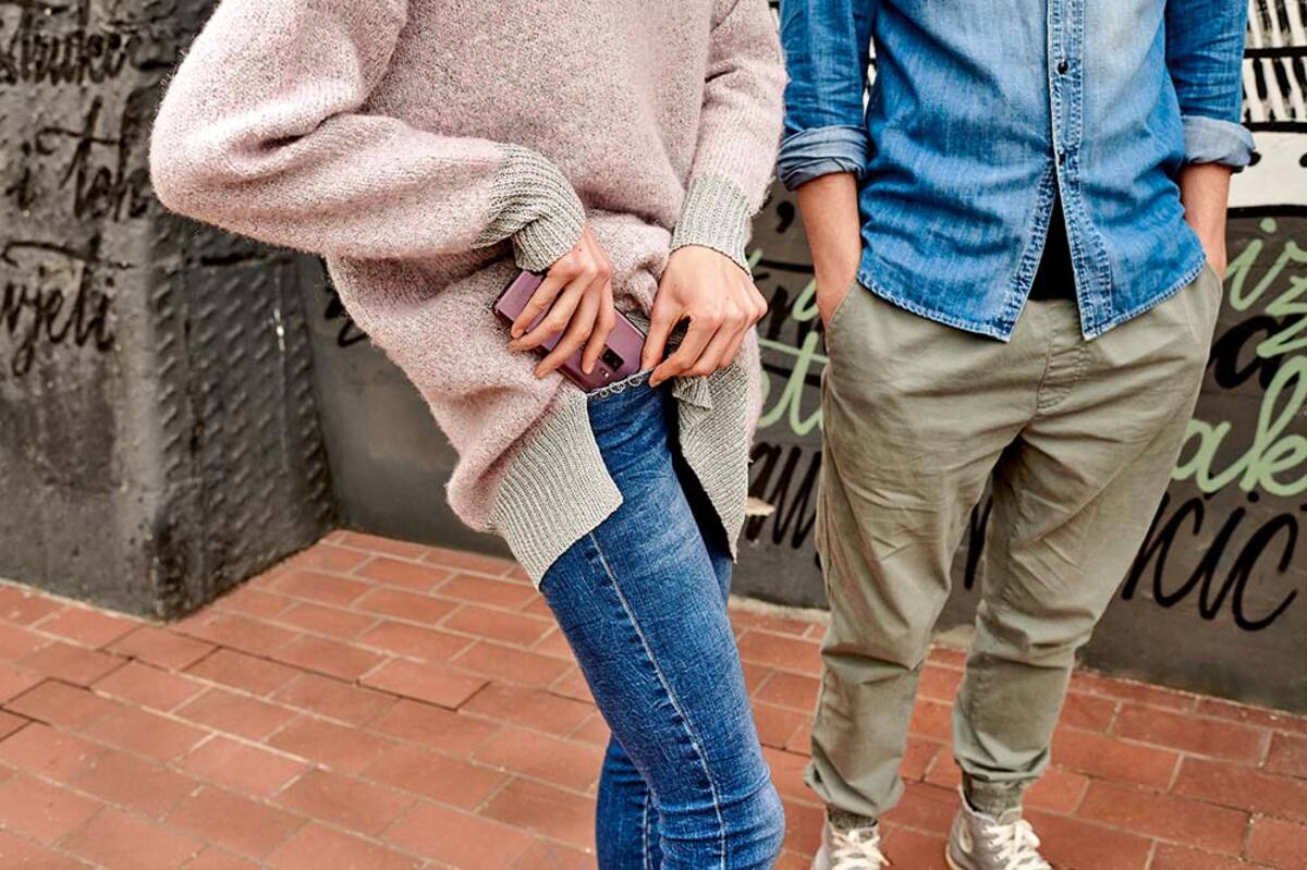 Kobieta chowa smartfon do kieszeni w spodniach